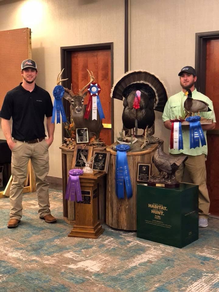 Cole and Hunter Mears with championship whitetail, turkey and duck mounts and rows of ribbons